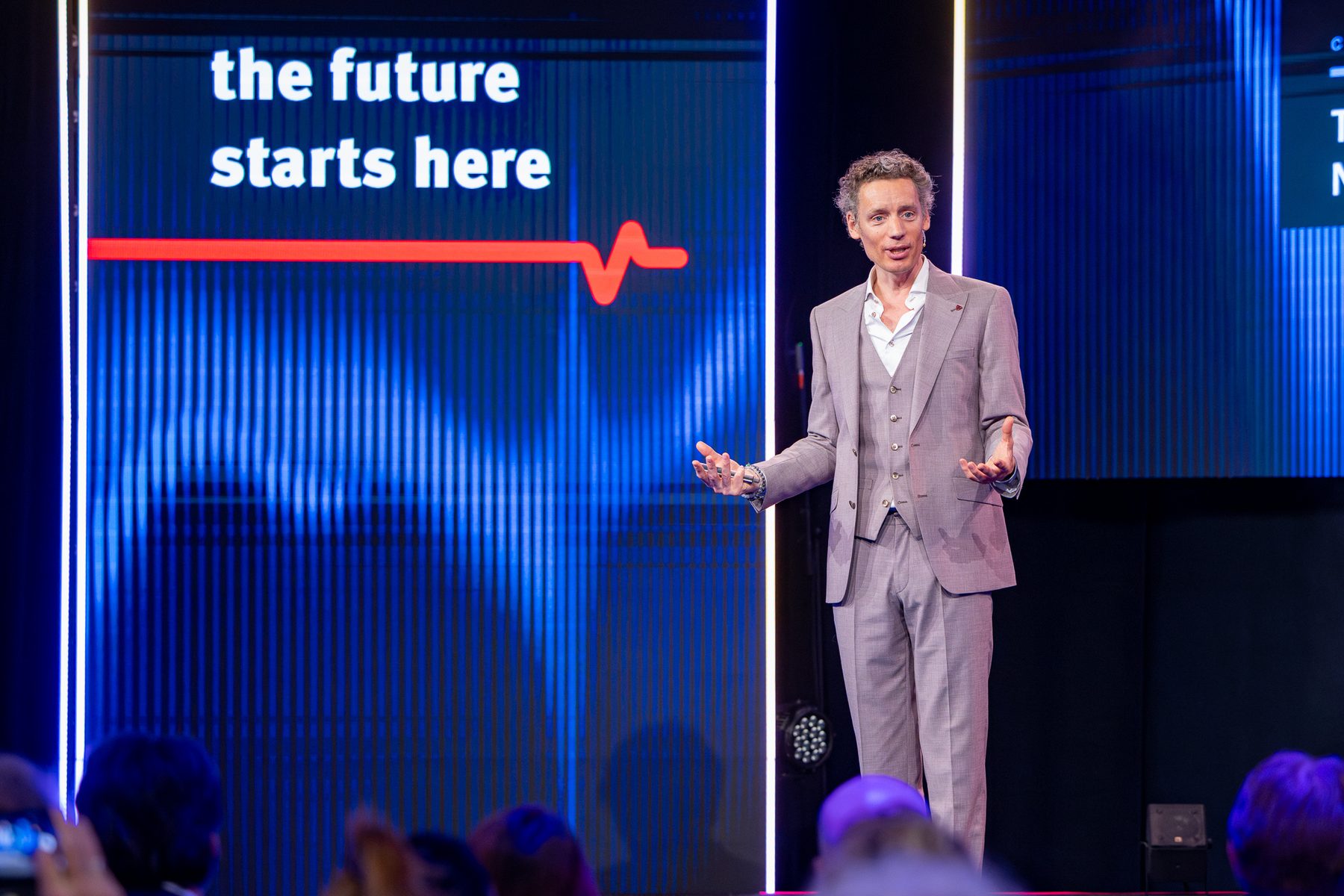 Laurens Waling in grijs driedelig pak op een blauw verlicht podium, naast een LED-wand met de tekst 'the future starts here'