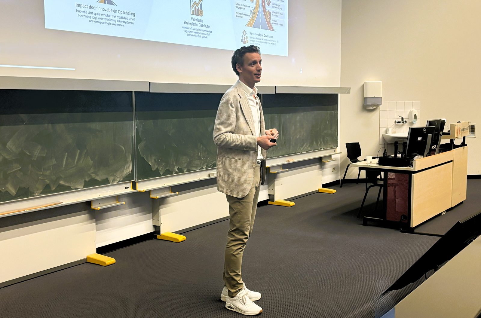 Laurens Waling geeft college in een zaal met groene schoolborden, voor een slide over impact door innoveren en opschalen